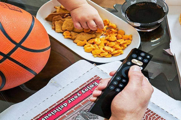 Snacks and a basketball are sitting on a table as someone is changing the channel with their Caavo remote