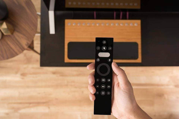 A hand is holding the Caavo remote with the Control Center box in the background