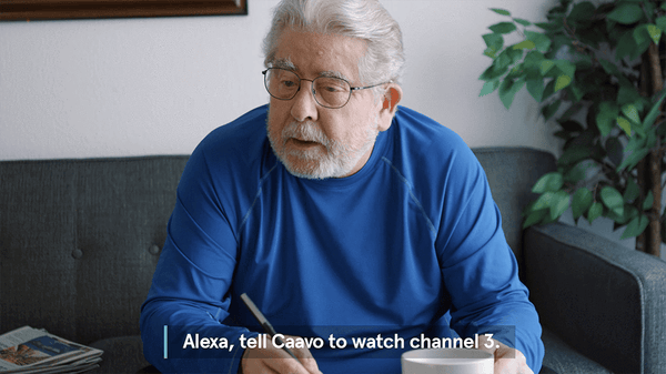 An old man in a blue shirt drinking coffee and talking to Alexa