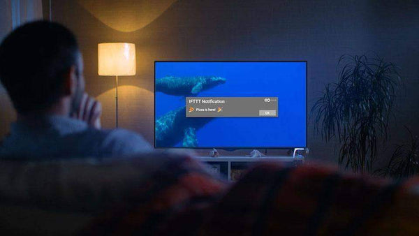 A man is sitting in his living room and using IFTTT with his smart TV