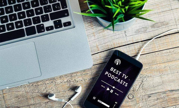 An iPhone that's displaying "Best TV Podcast" lays next to a Macbook and a succulent 