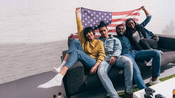 Four young friends are posing in front of a couch while holding the American Flag 