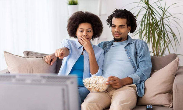 A male and female couple watching TV and eating popcorn